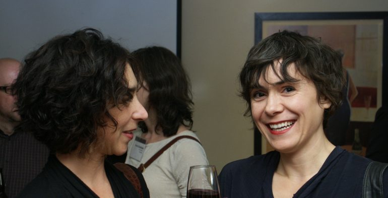 Two short haired women talking, one smiles at the camera