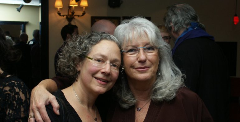 Two grey-haired, radiant women smiling at the camera