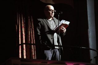Man wearing glasses reads at a microphone