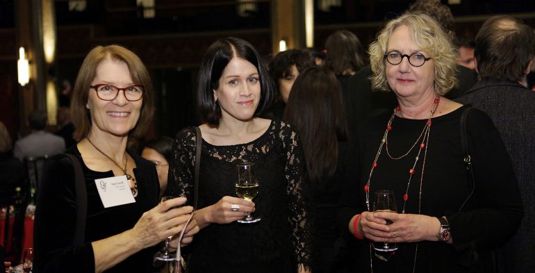 Three women with drinks wearing black and smiling